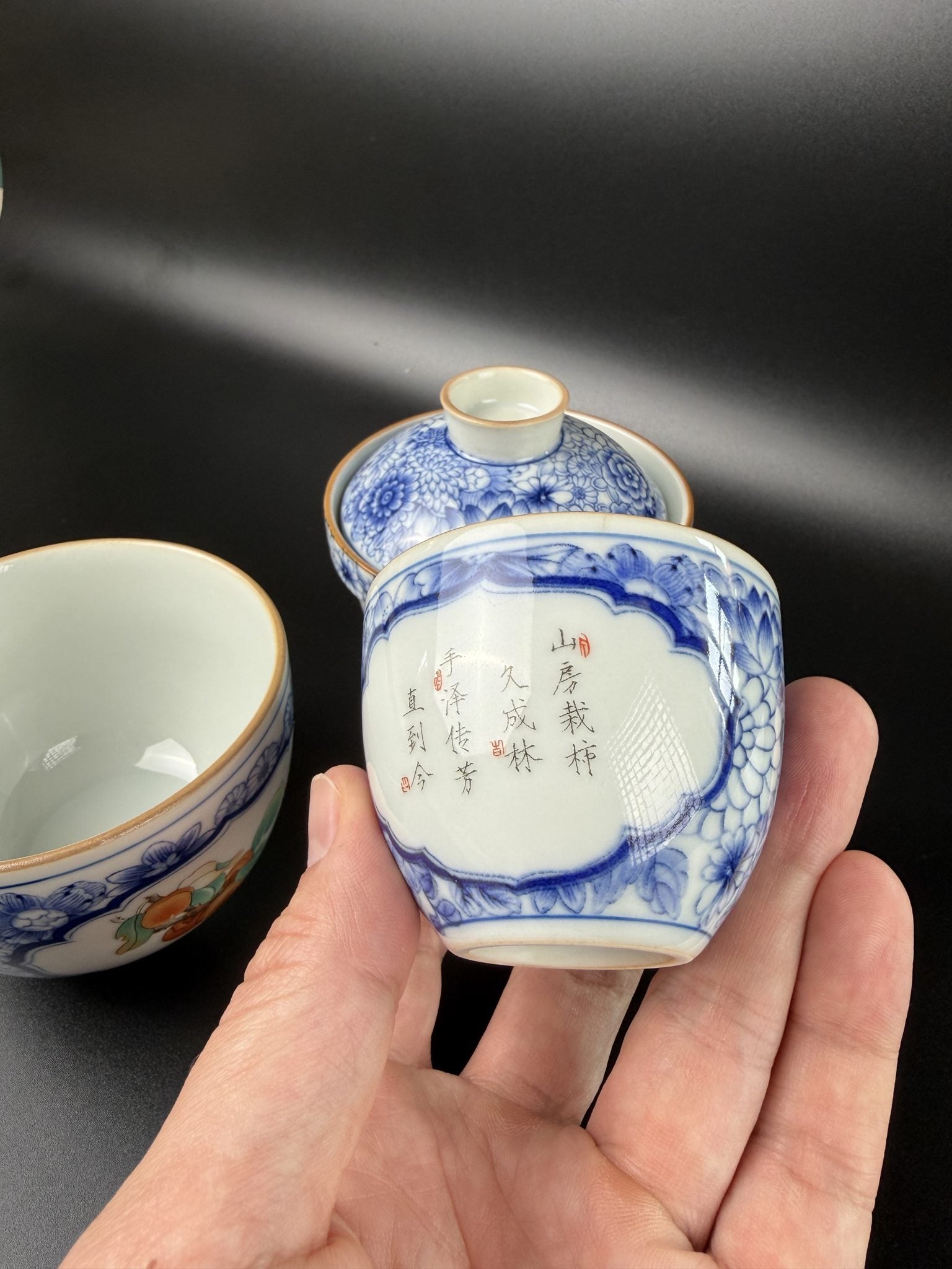 Petite tasse calligraphiée du service de voyage Daothé tenue en main, porcelaine fine bleu et blanc